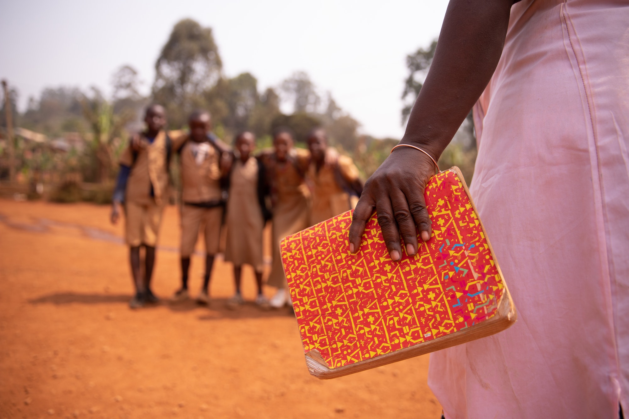 An african teacher is holding a book with her students in the background, education in Africa